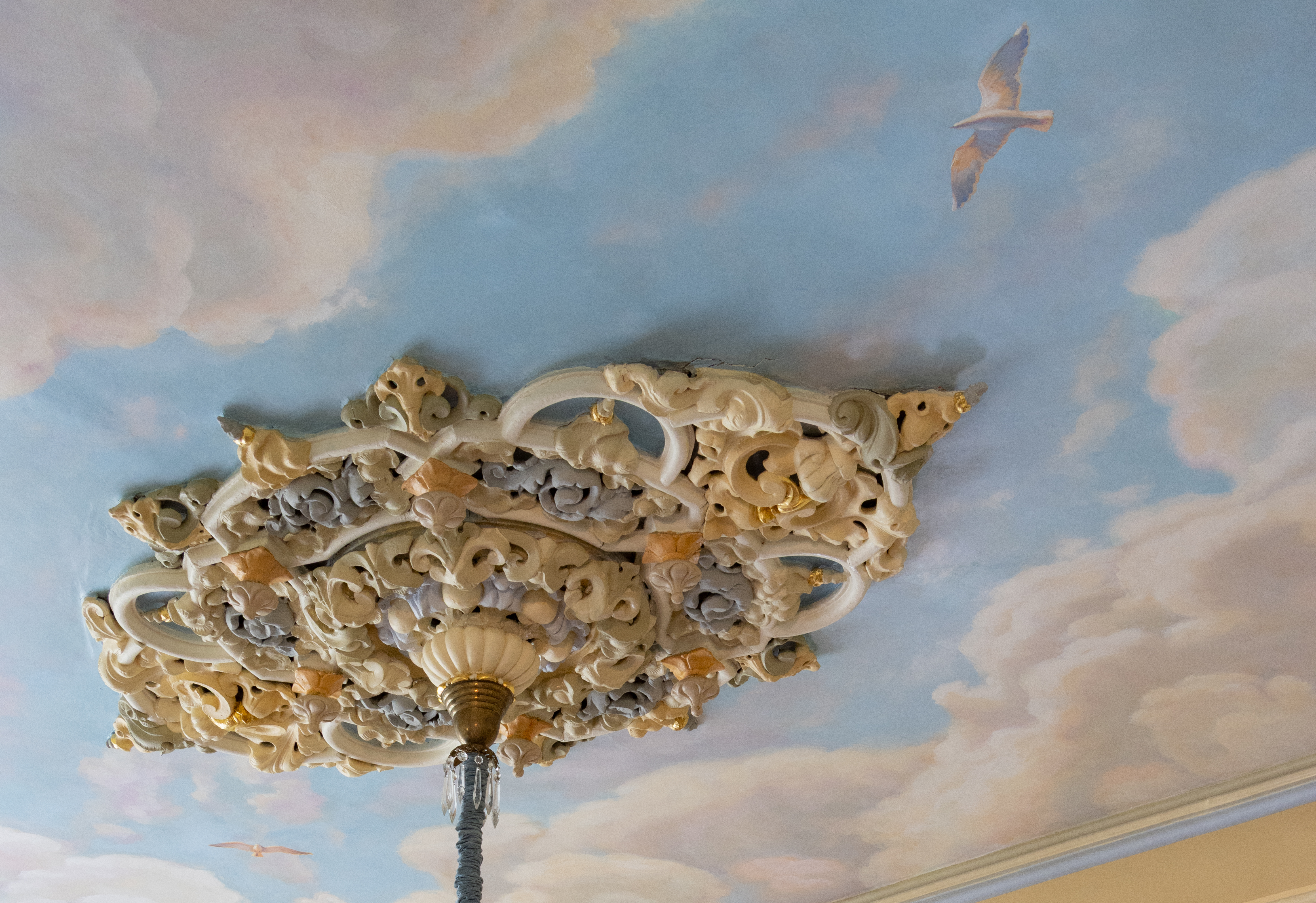 a multi-colored ceiling medallion and a ceiling painted with clouds and birds