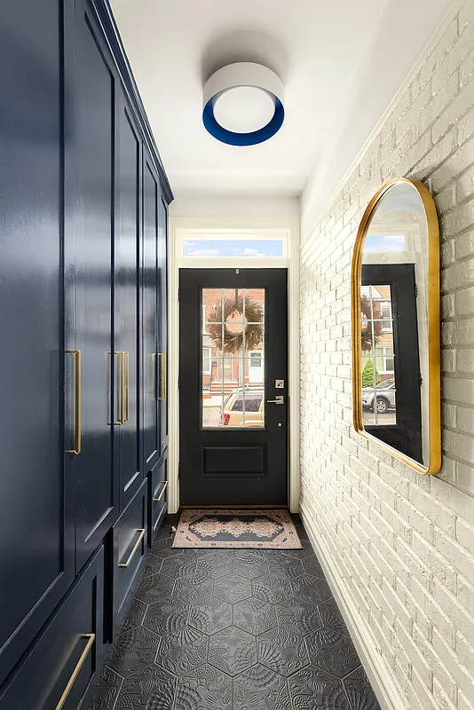 entry with painted brick wall, blue-painted wall of storage, and black hex floor tile