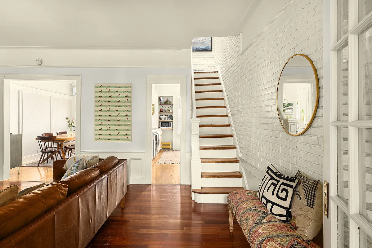 view of living room from entry with a wall of white-painted brick and a staircase