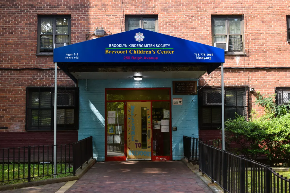 a red brick building with a royal blue trianglular awning reading brefvoort children's center. the door frame is painted red with a thick light blue boarder