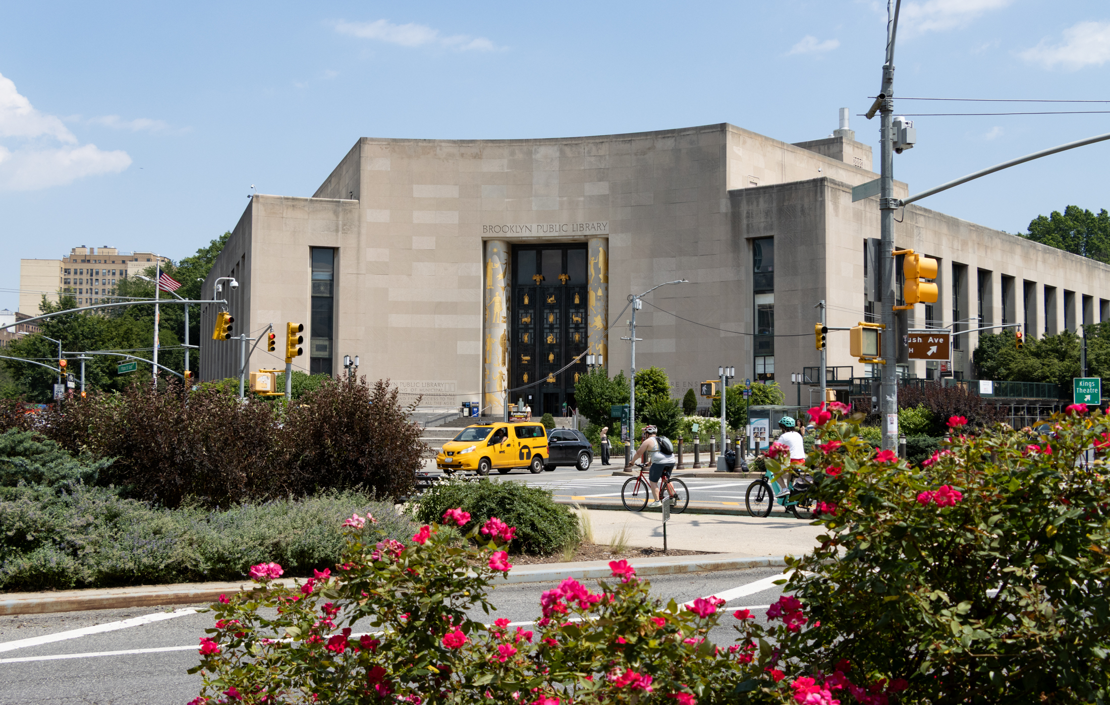 roses blooming in the foreground with cyclists and cars in front of the brooklyn public library