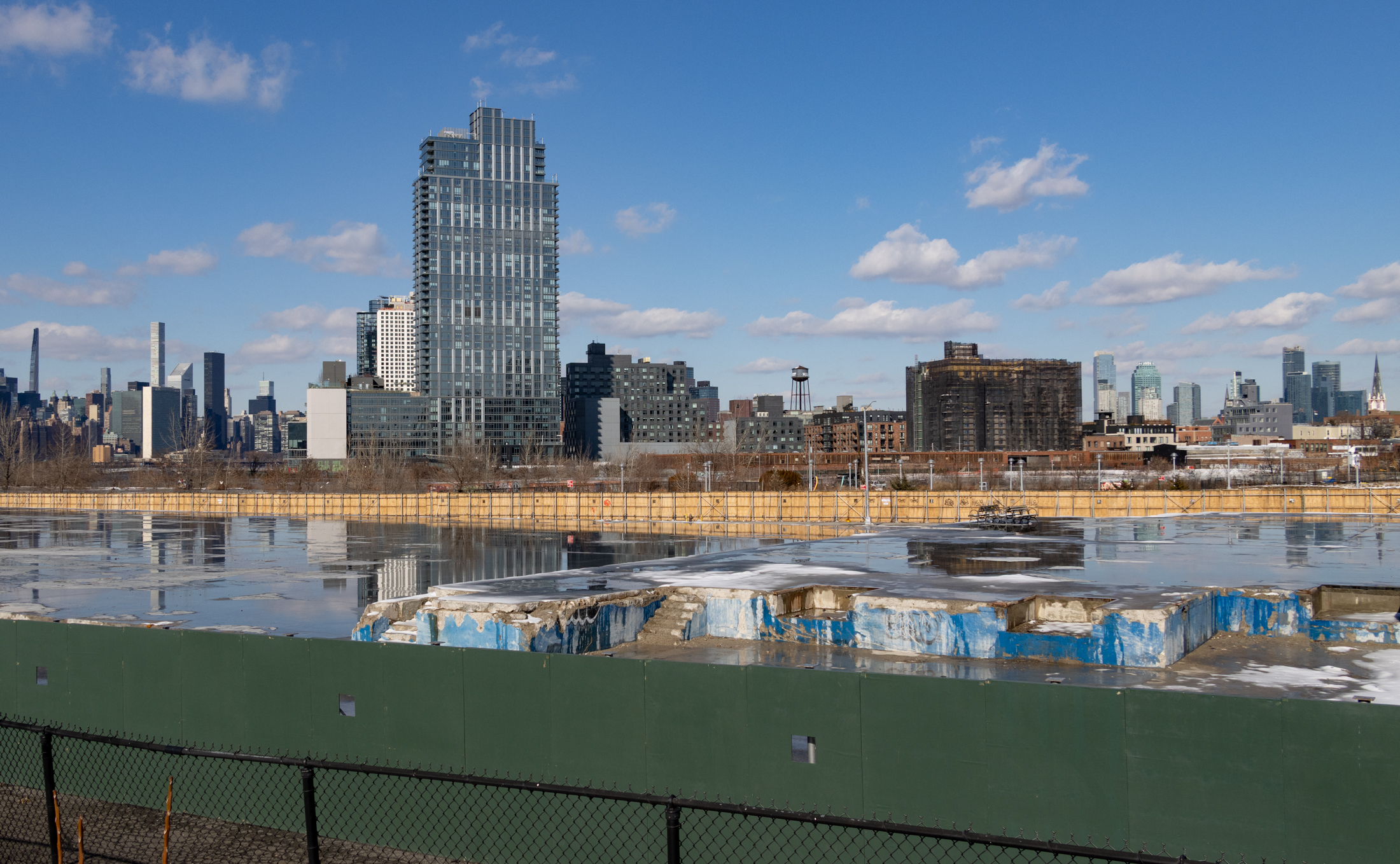 green construction fence with a building almost completely demolished and the project site beyond