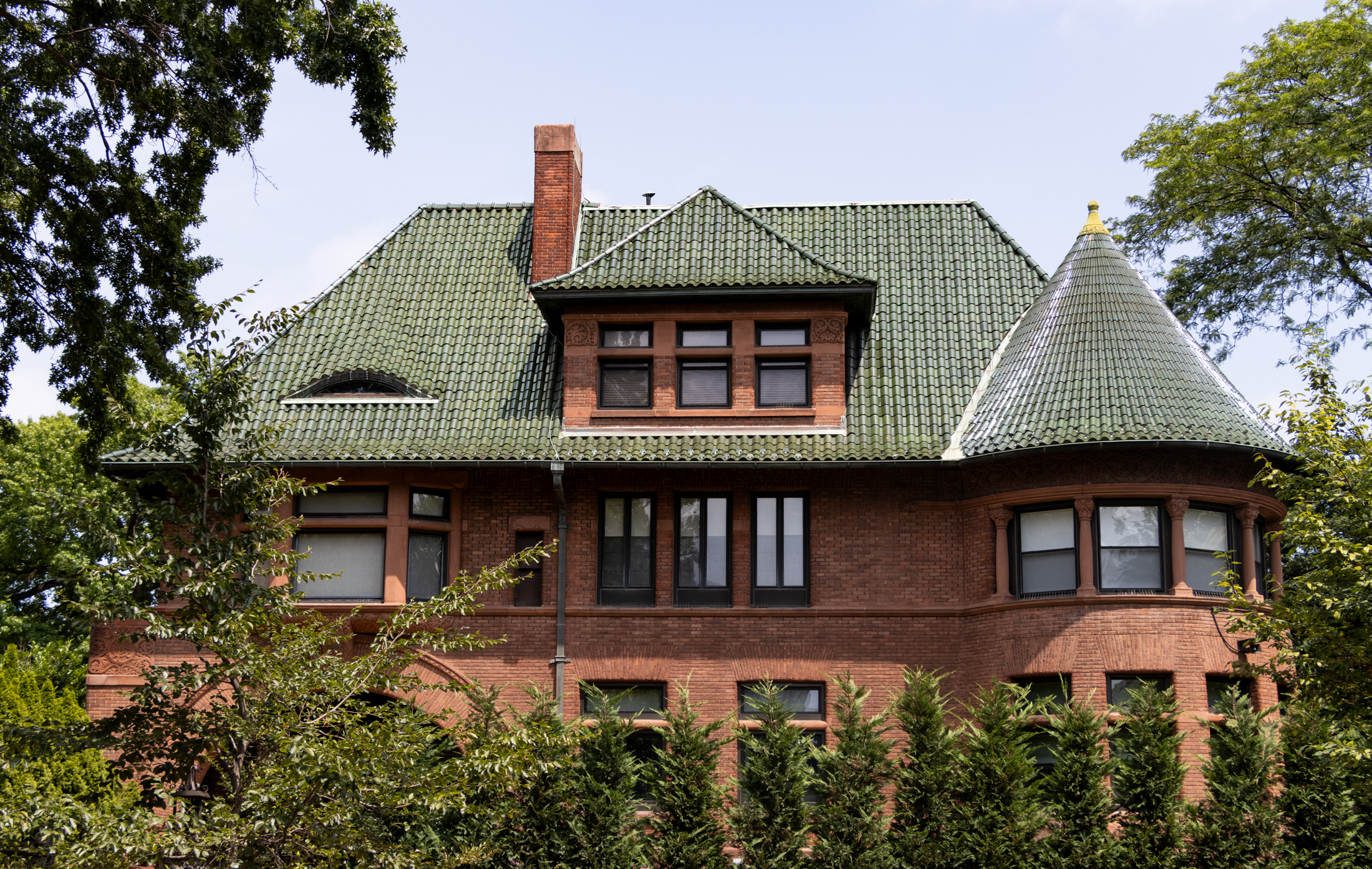 a red brick mansion with a green tile roof in clinton hill