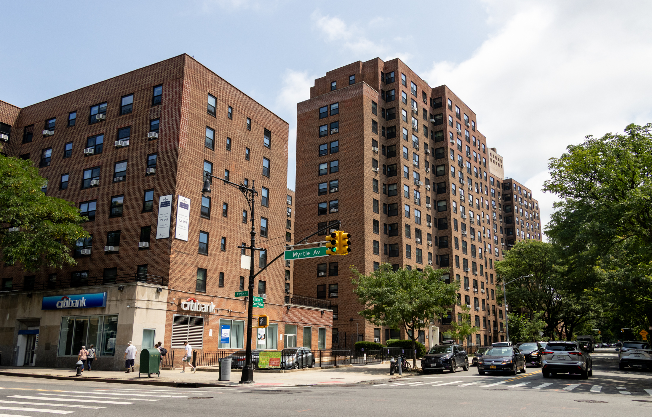 pedestrians and traffic on streets in front of tall brick apartment buildings