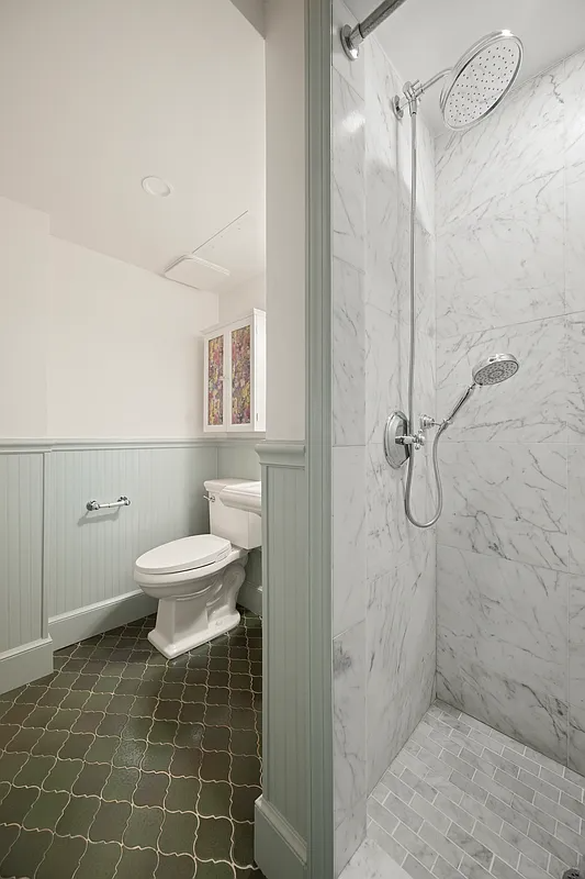 bathroom with beadboard, white fixtures and a shower with marble tile