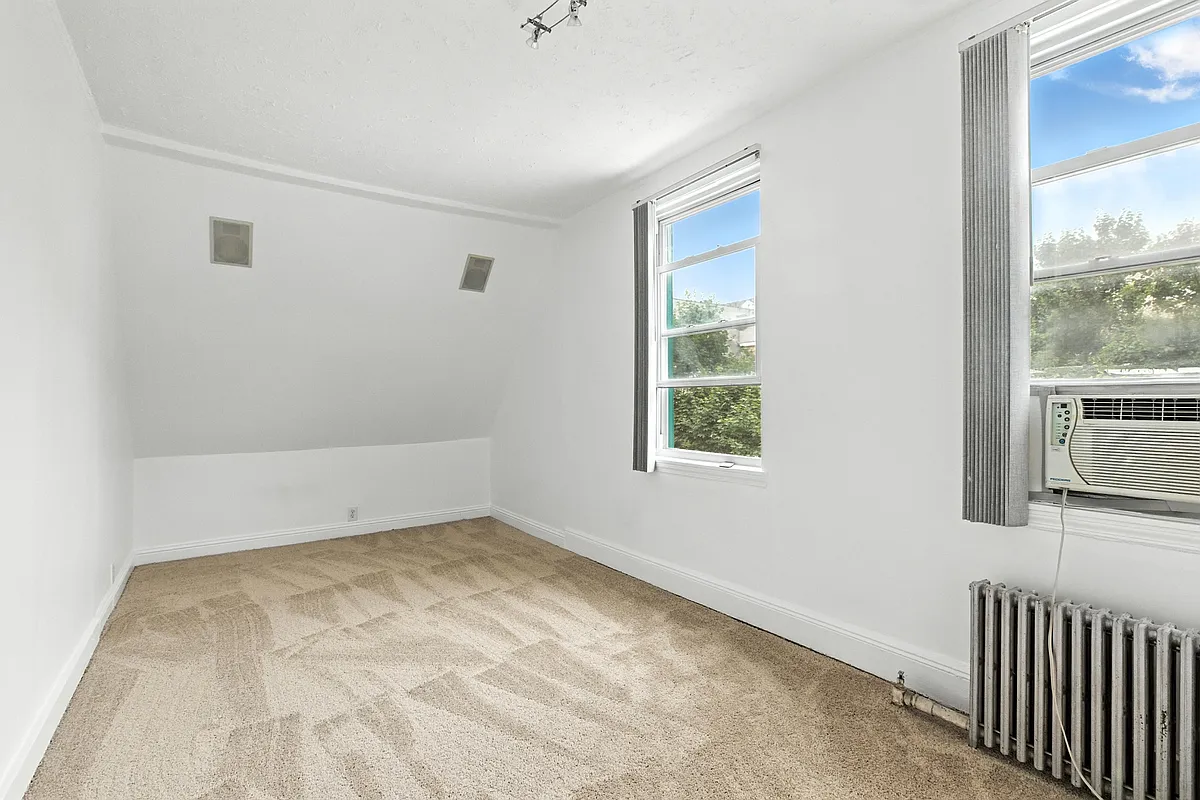 a bedroom with beige carpet, two windows, and white walls