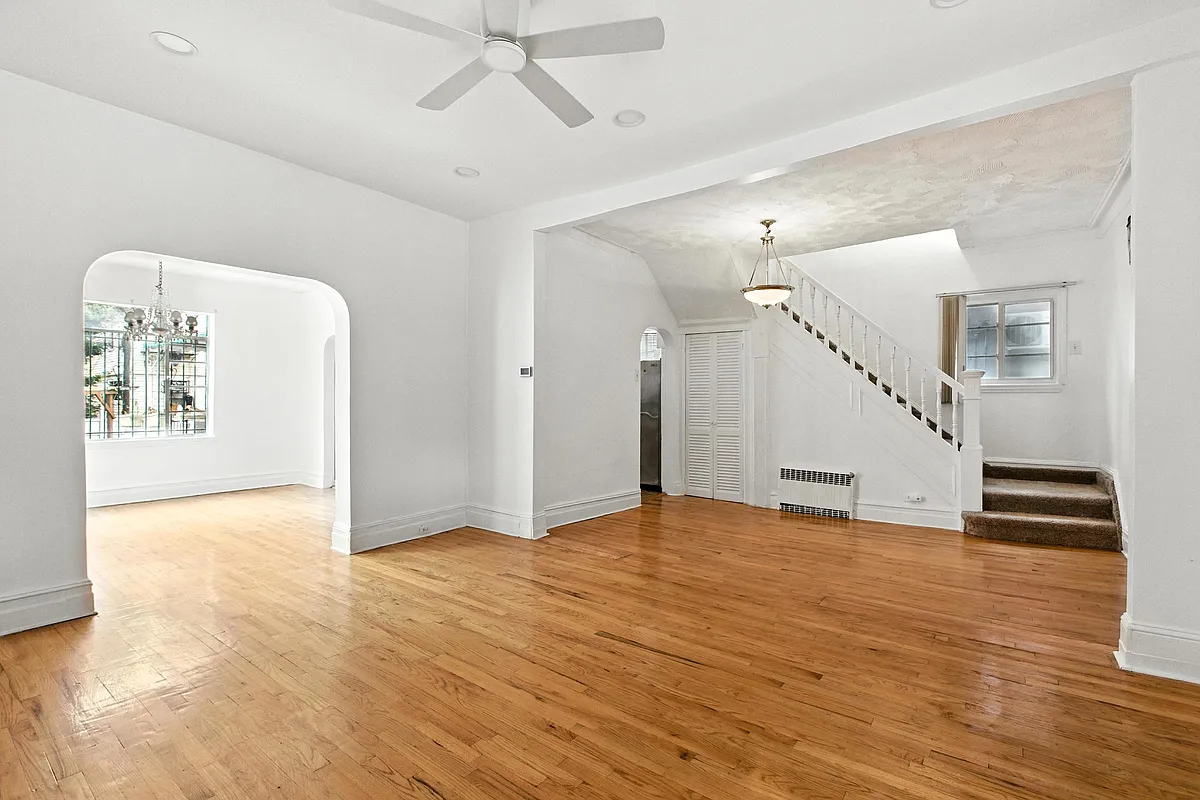 a living room with white walls, a wood floor, arched doorways and a view to the stair