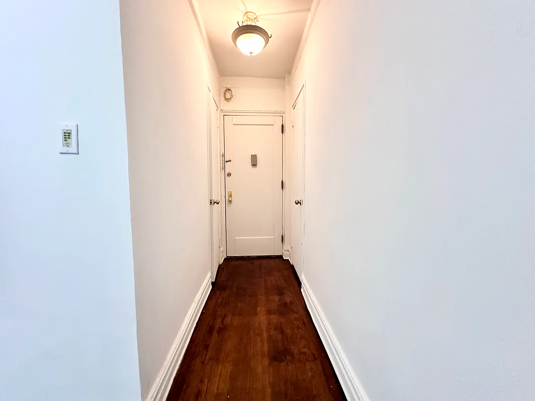 hallway to front door with wood floor, white walls