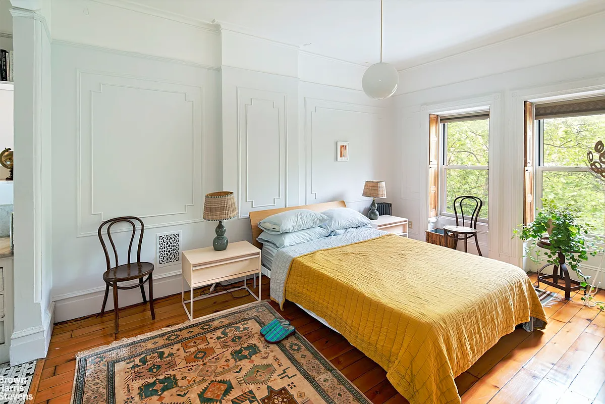 a bedroom with wall moldings, a wood floor, and interior window shutters