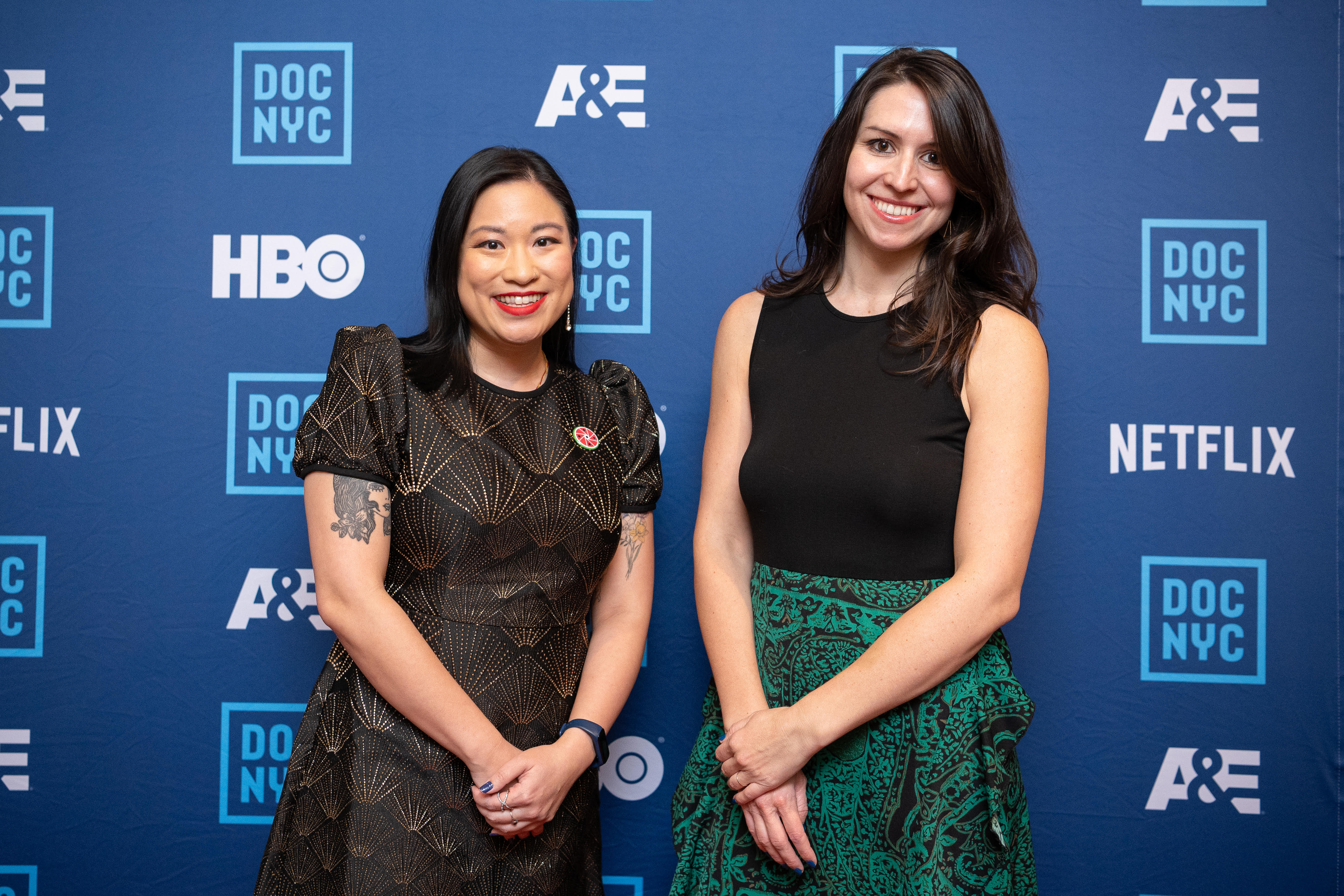 two women pose in front of a blue step-and-repeat background
