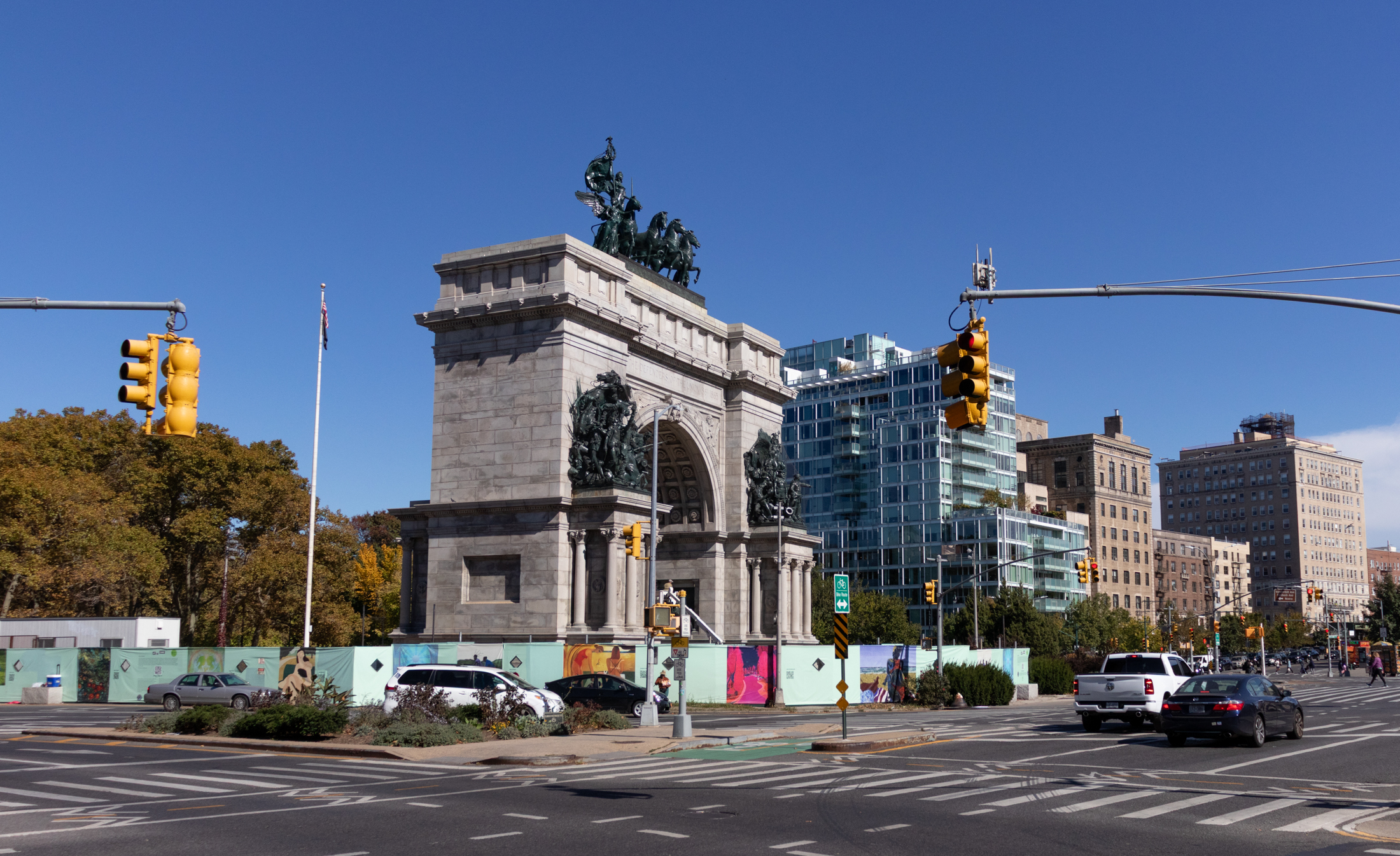 cars driving by a construction fence surrounding the memorial arch
