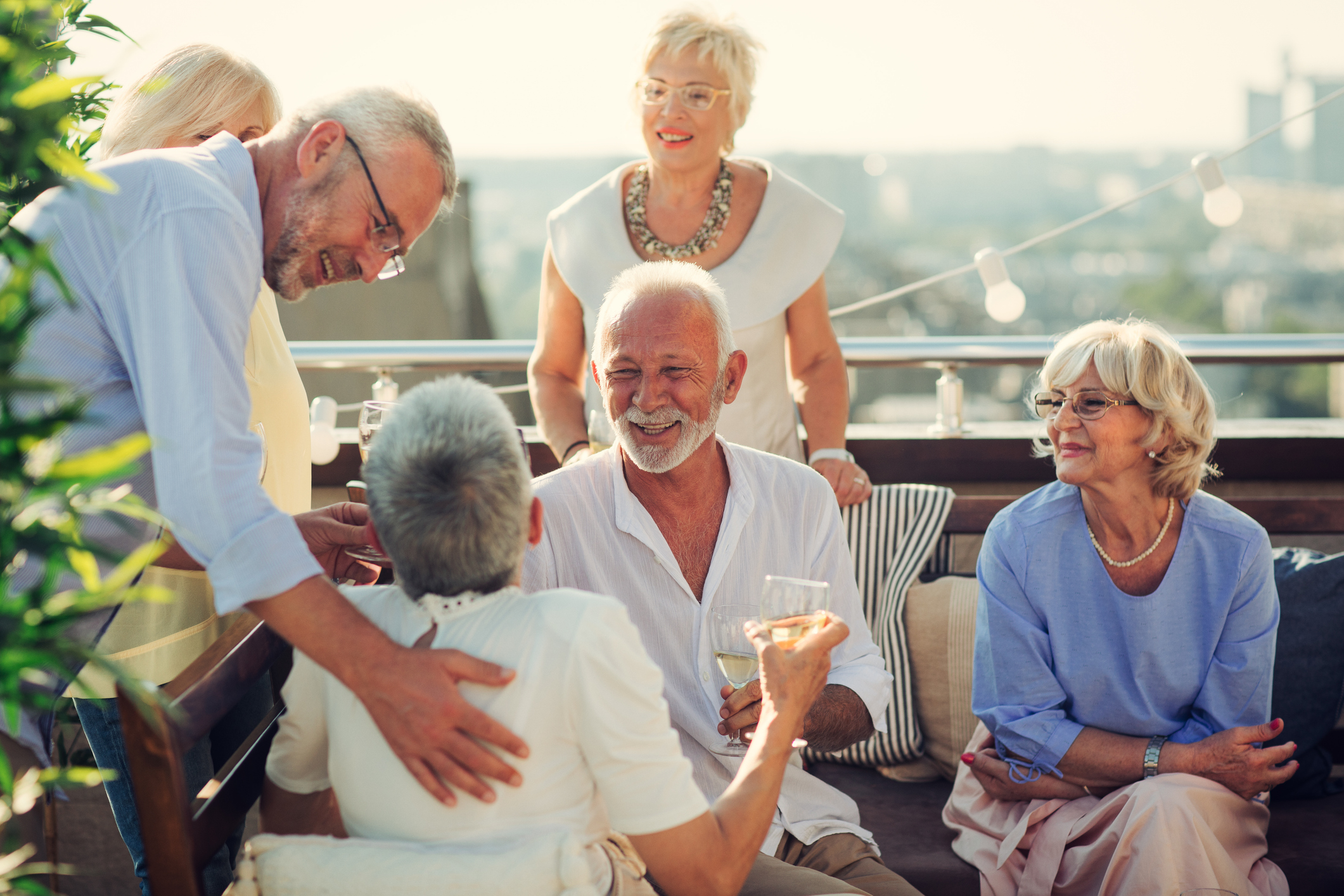 Group of senior friends having fun on rooftop terrace together. Sitting, talking and drinking champagne.