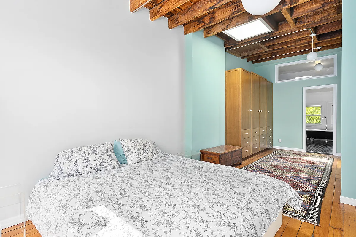 bedroom with exposed rafters, a skylight, and an ensuite bath