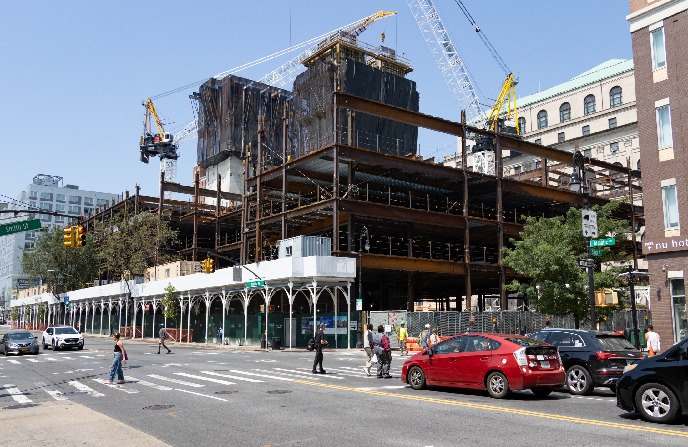 people crossing atlantic avenue with the steel framework of a building rising behind them