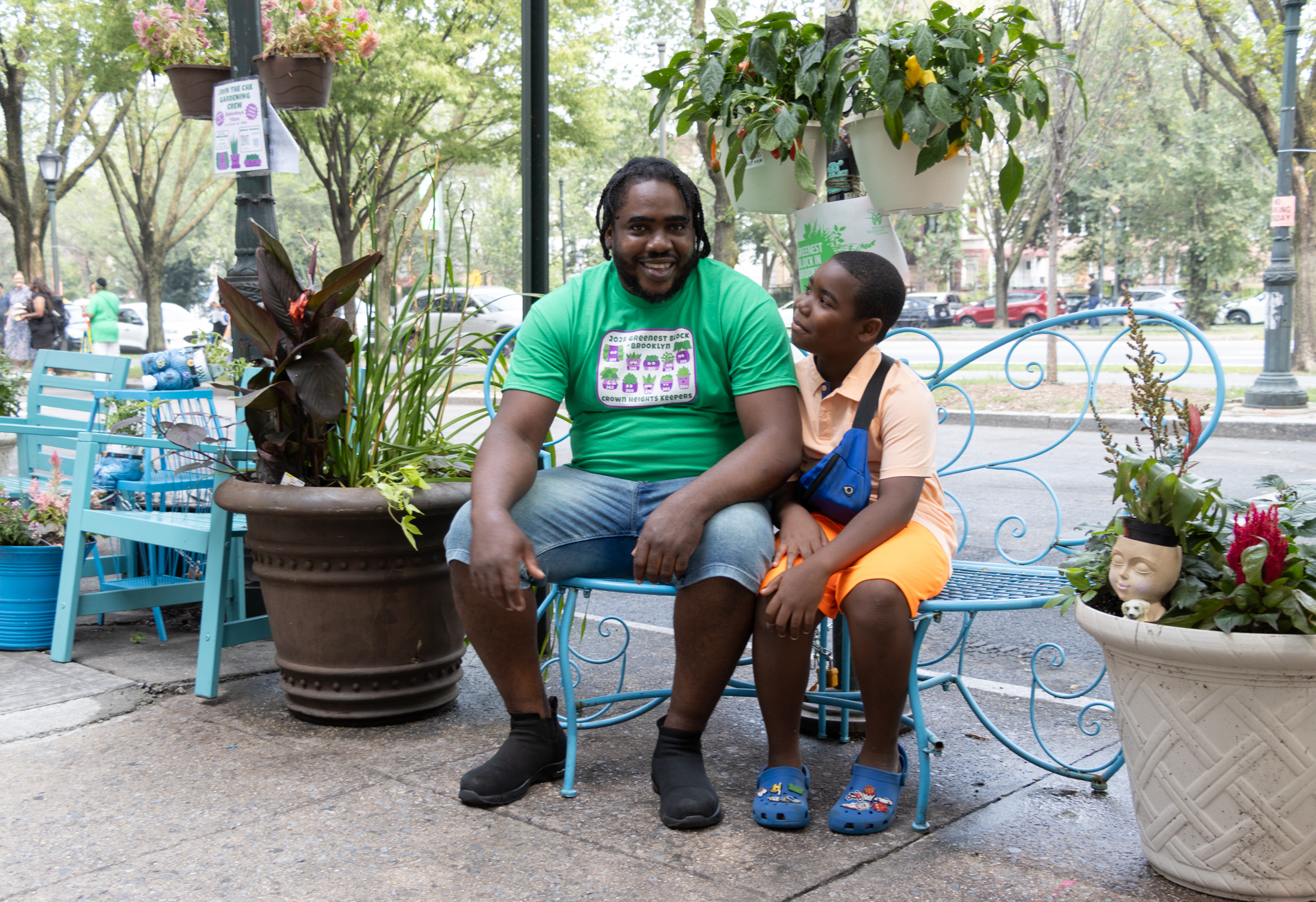 a father and son pose on a blue bench with planters on either side