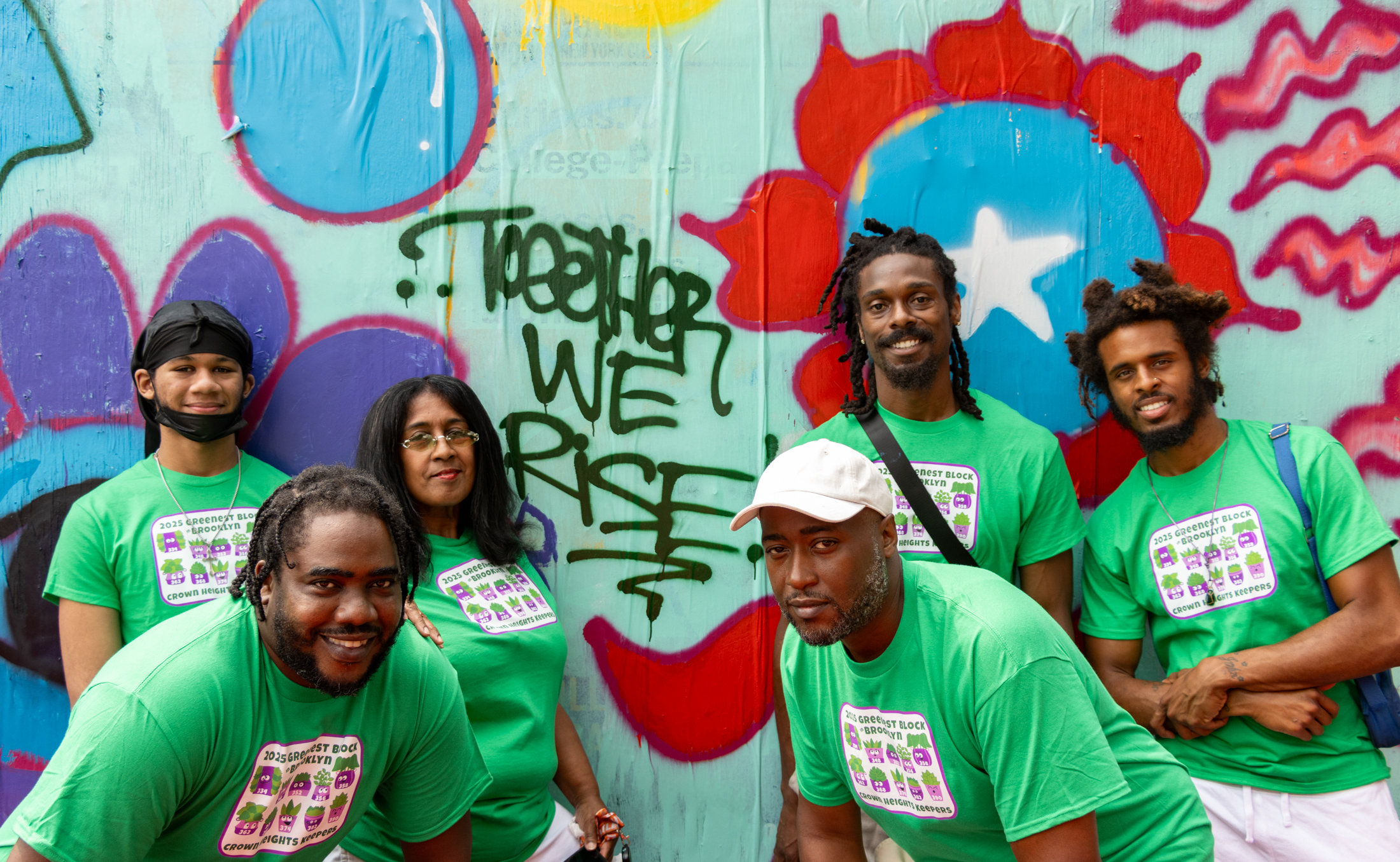 group of neighbors in matching greenest block tshirts posing in front of a mural