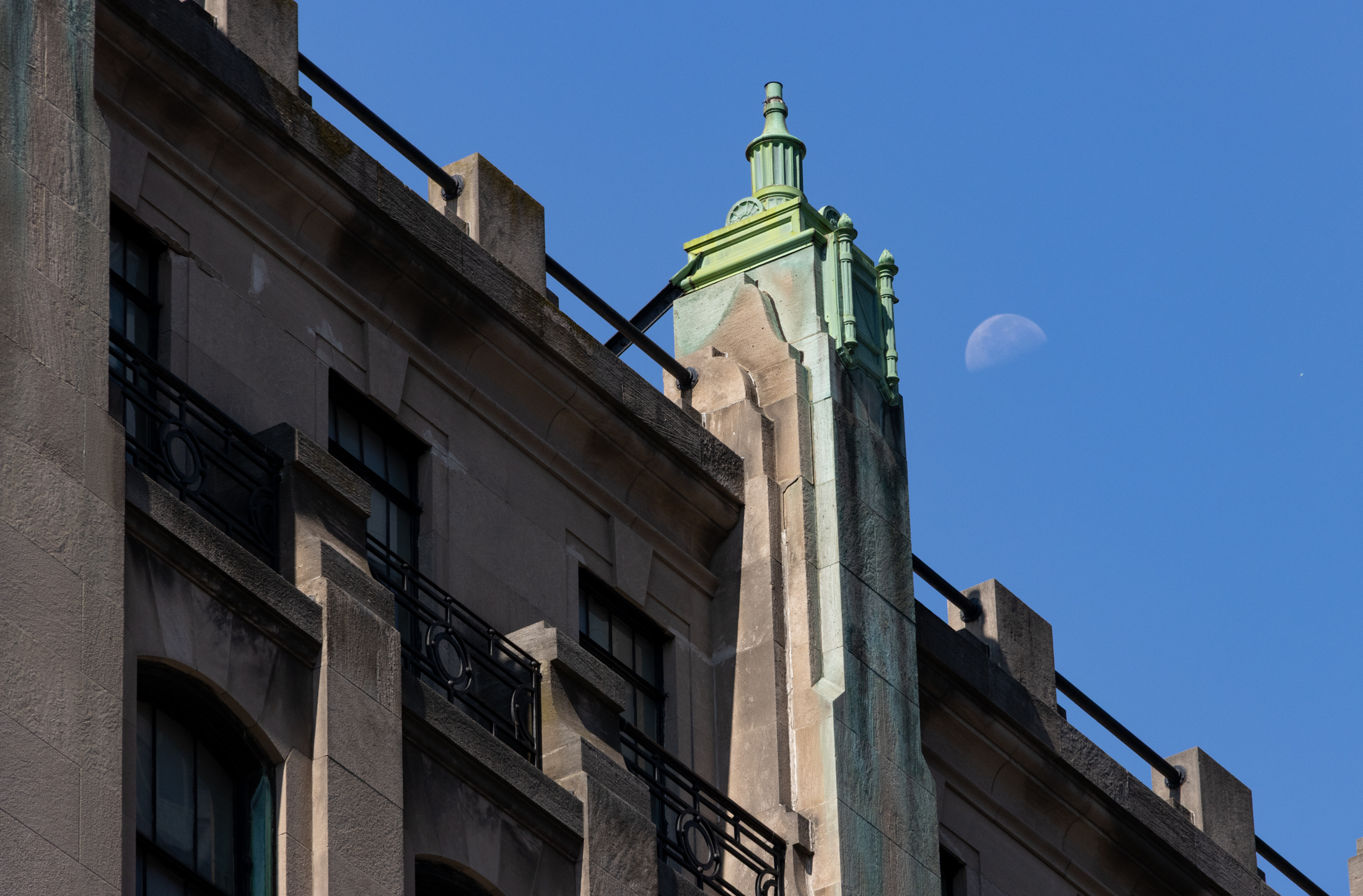 a rooftop detail with copper ornament with a green patina and a glimpse of the moon in the sky
