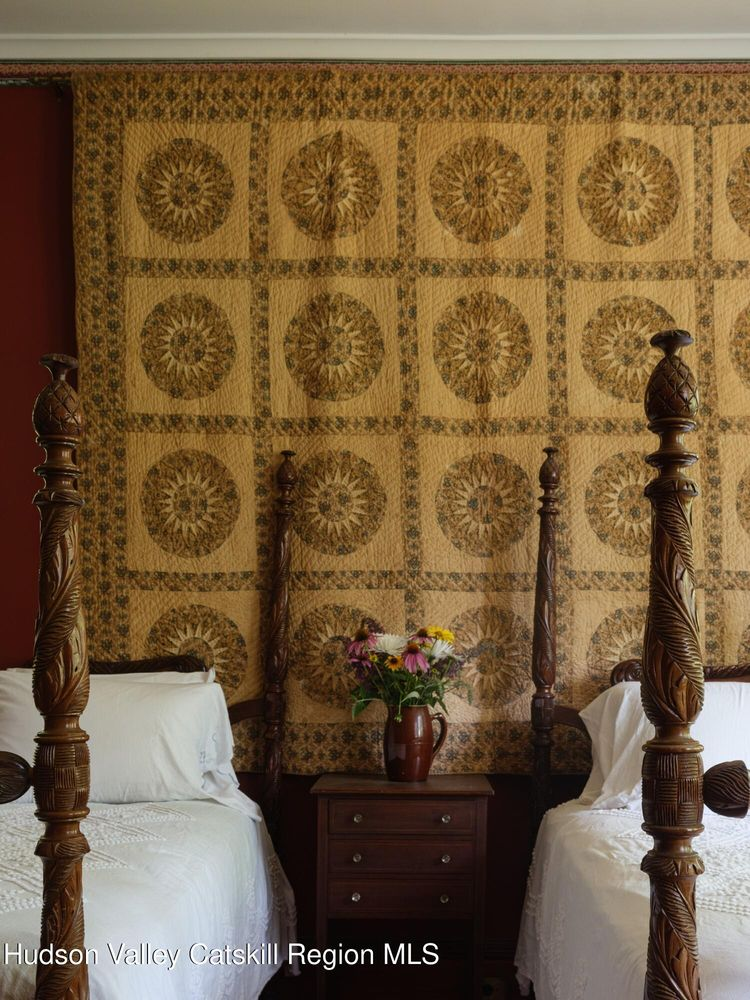 detail of a bedroom with two beds, a quilt hanging on the wall