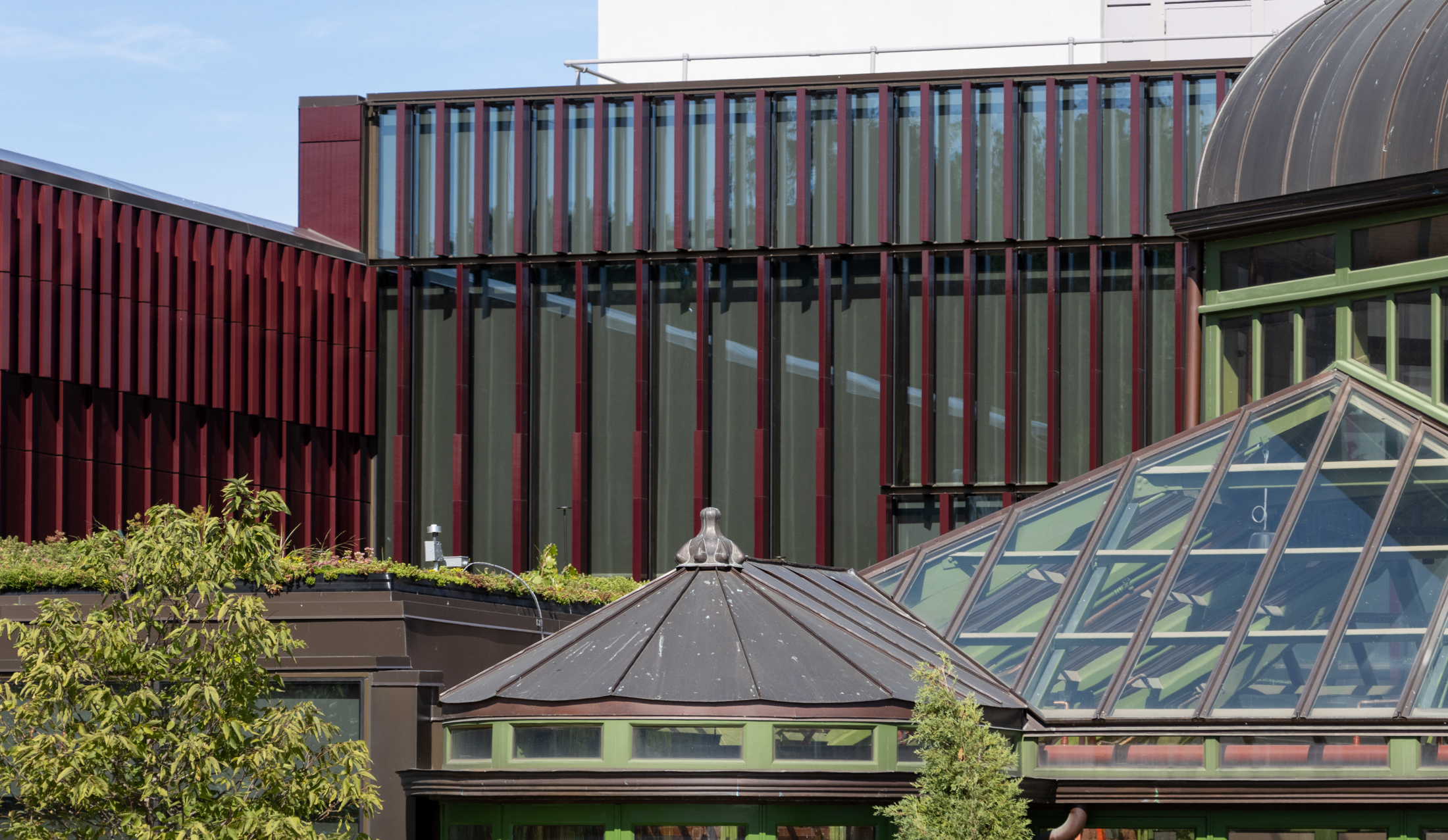 the restored greenhouse with green metal and the terra cotta slats of the modern building behind