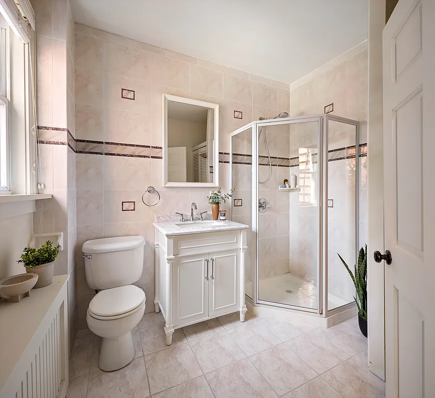 bathroom with beige wall and floor tile and a corner shower with glass walls