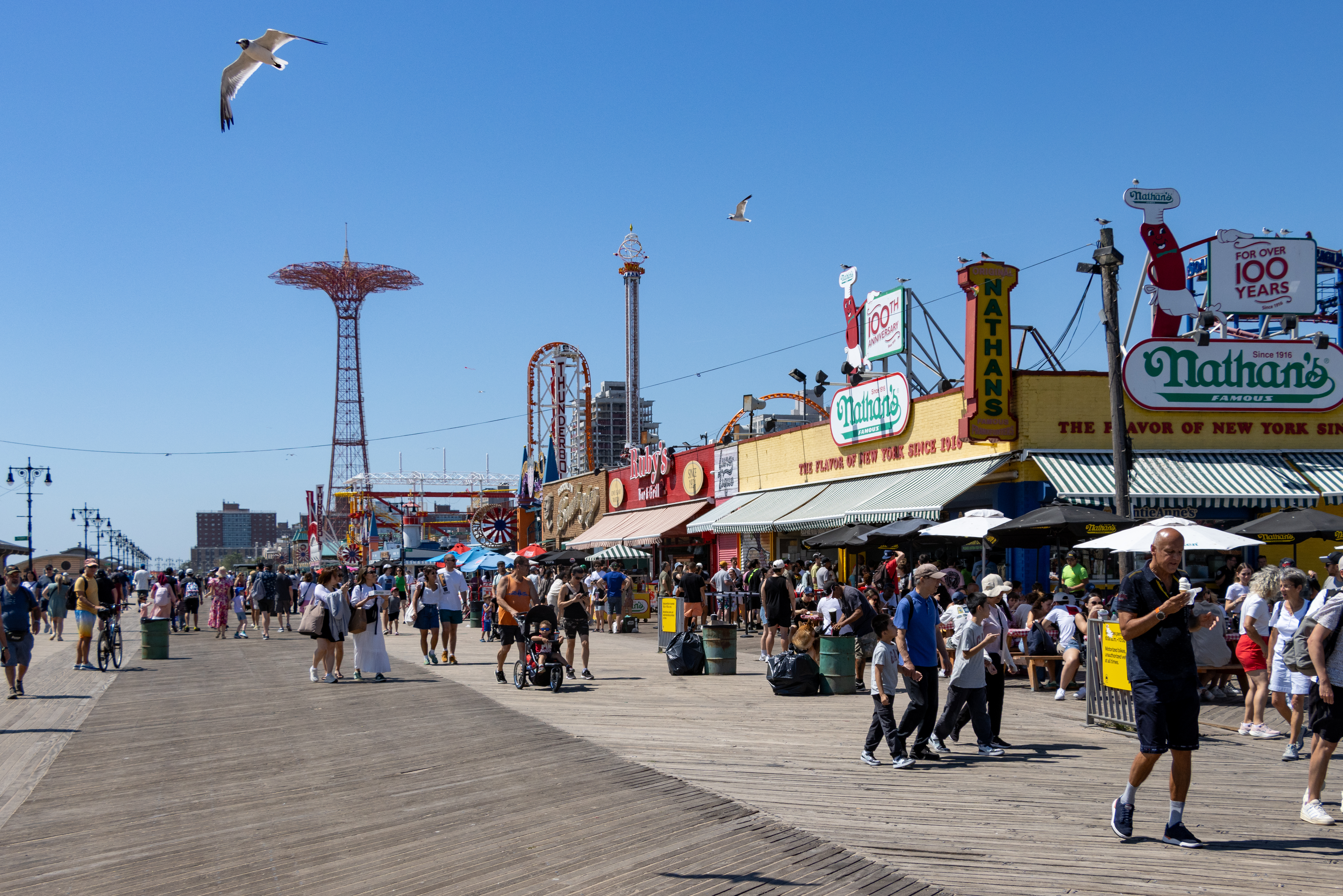 people on the boardwalk with the parachute jump in the background