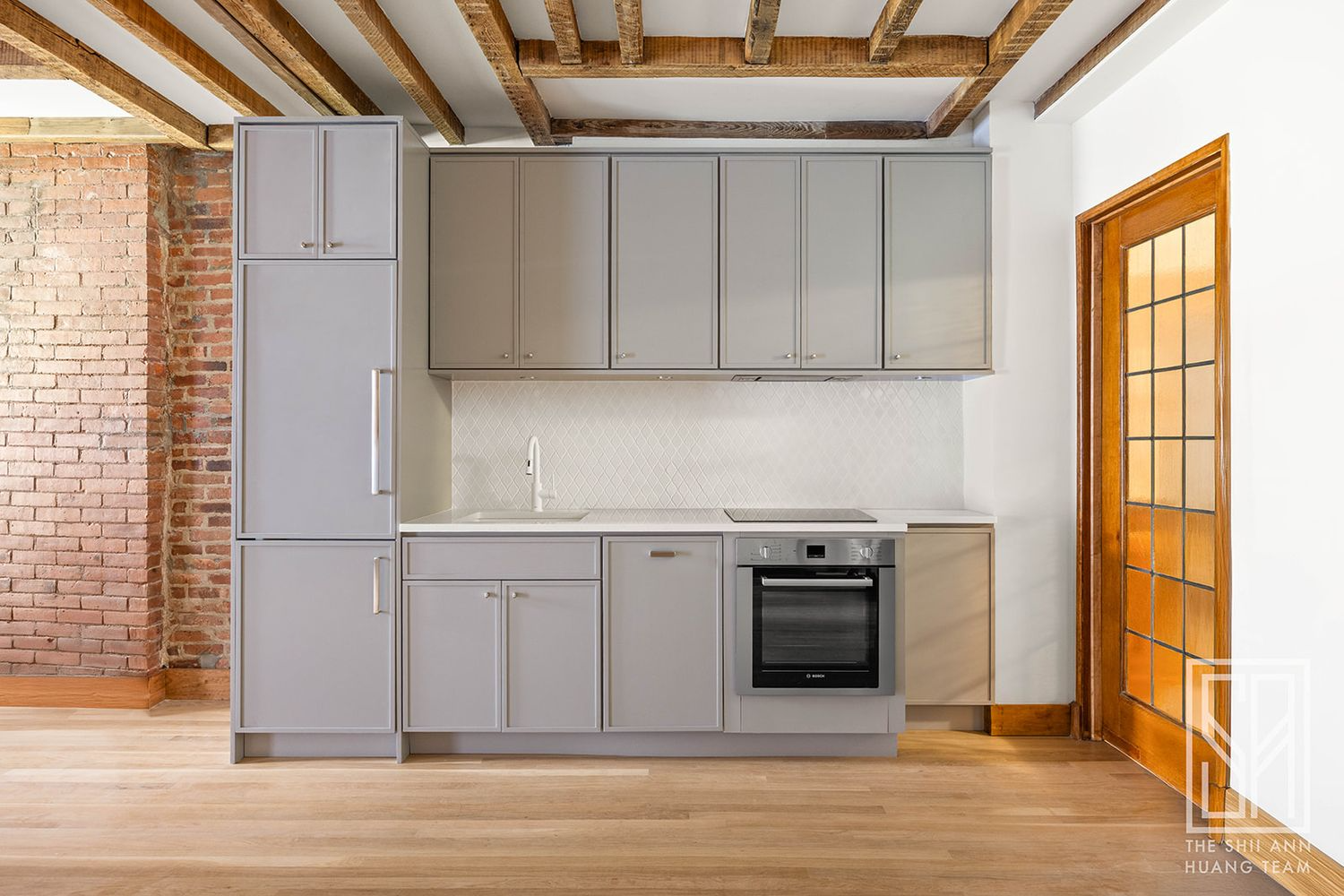 garden level kitchen with one wall of gray cabinets that includes the fridge faced with doors