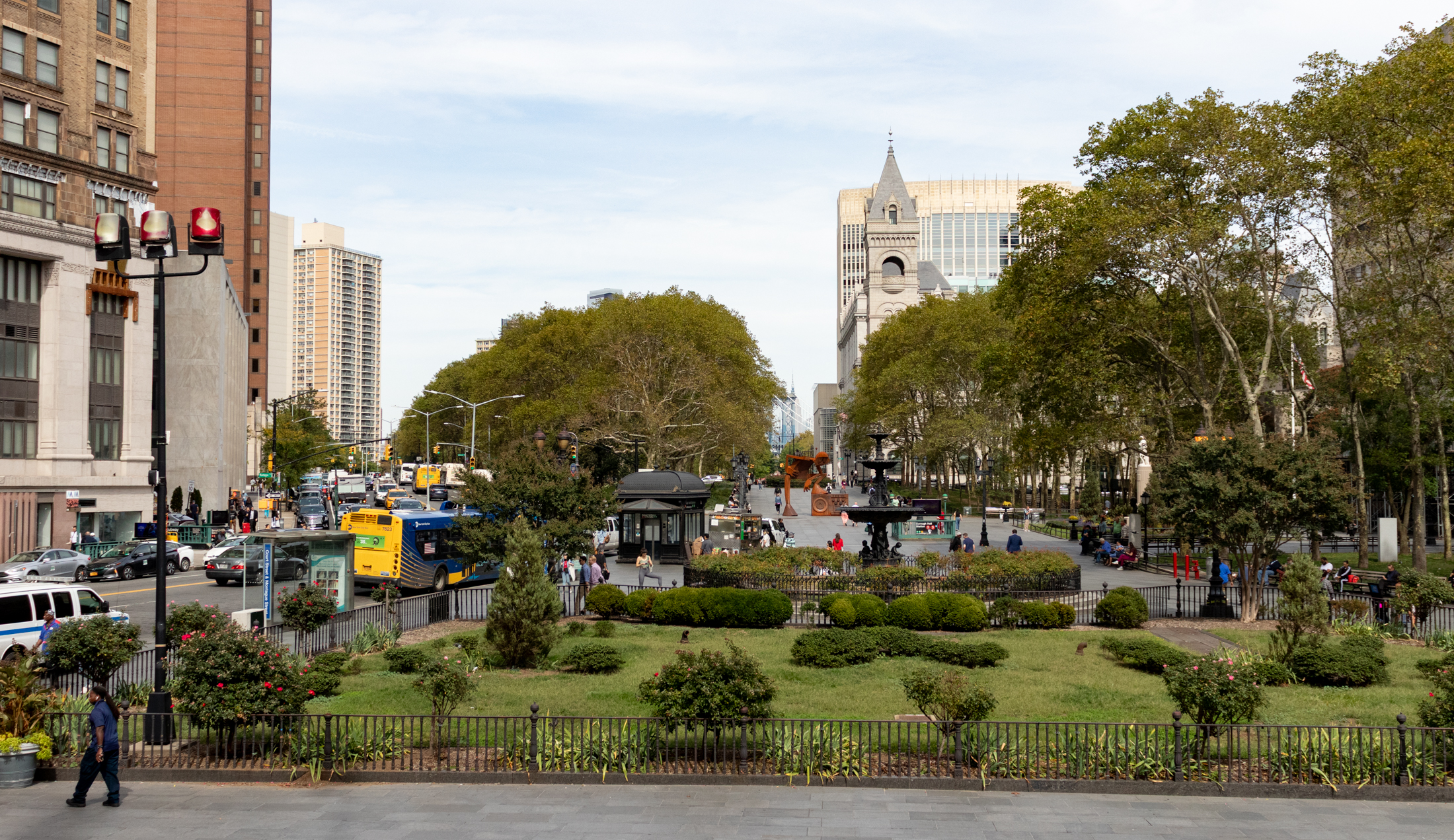 view of columbus park with greenery and pedestrians walking and the old post office in the background
