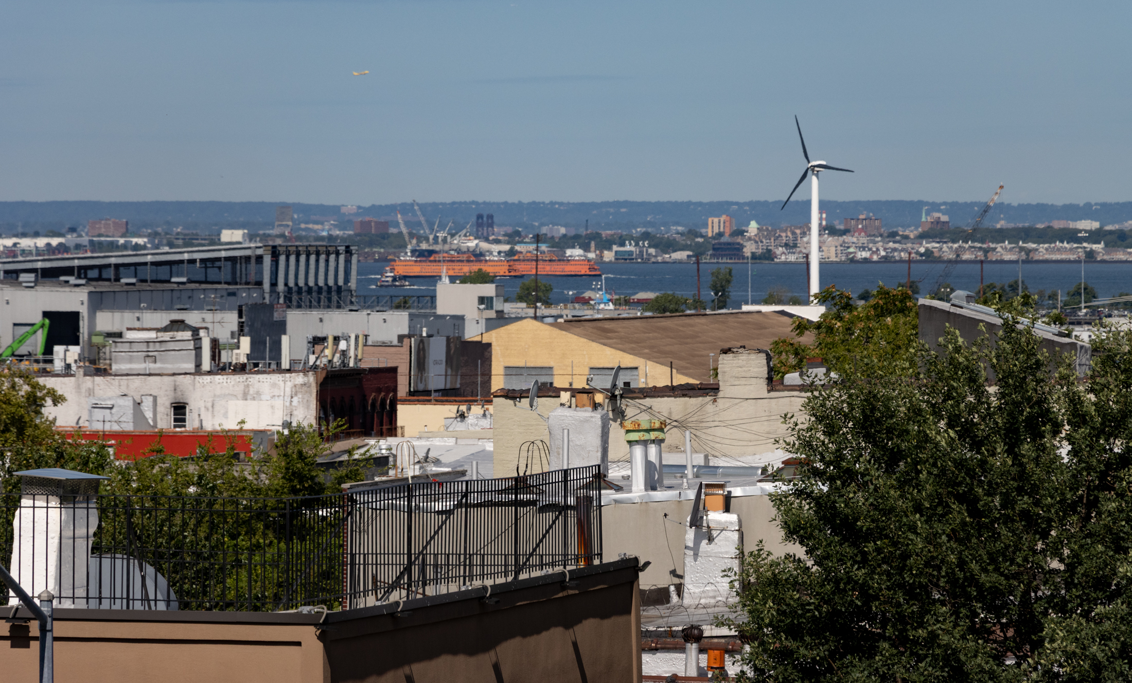 rooftop view looking to the water with a wind turbine and a staten island ferry in the distance