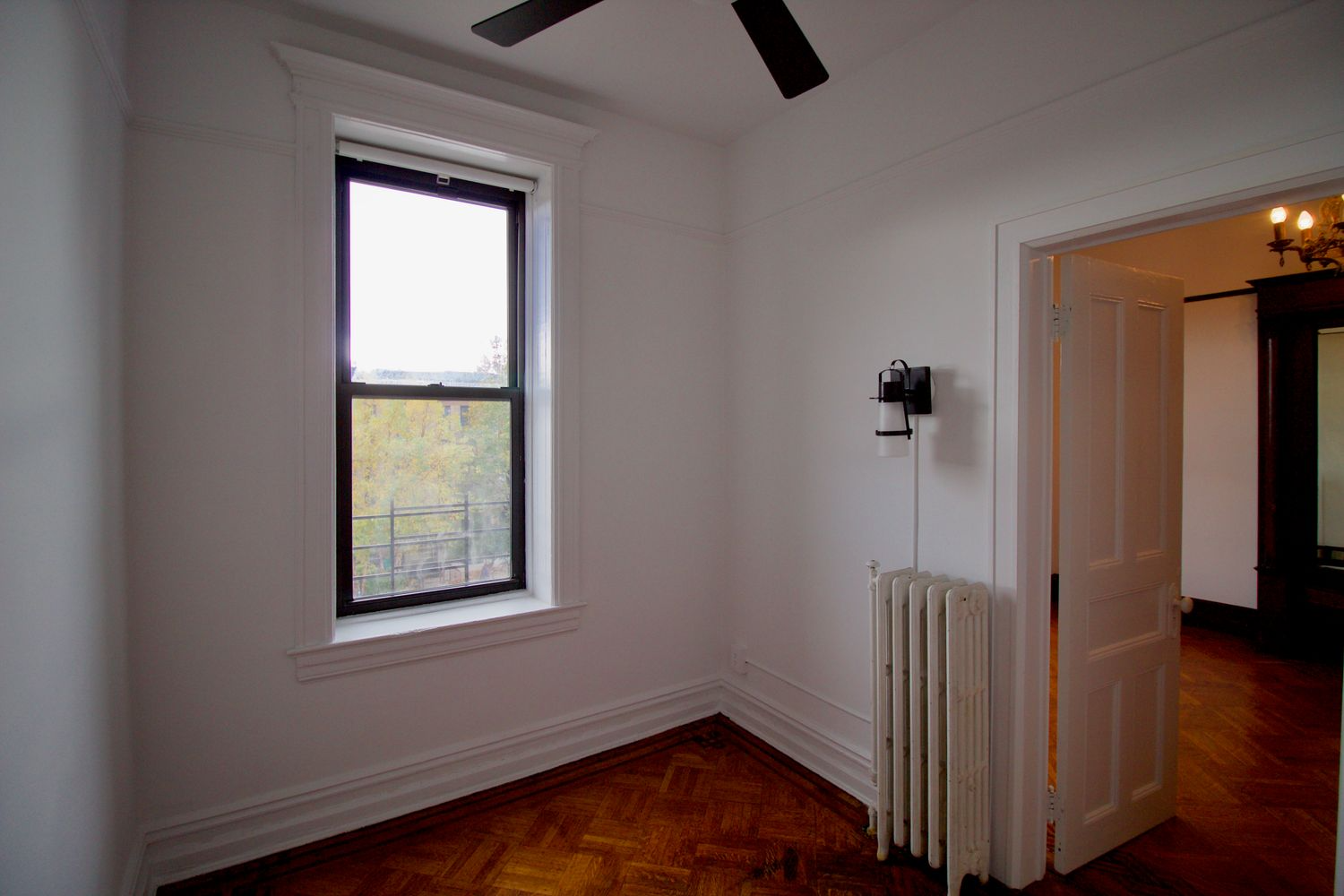 bedroom with white walls, wood floor, door opening into parlor
