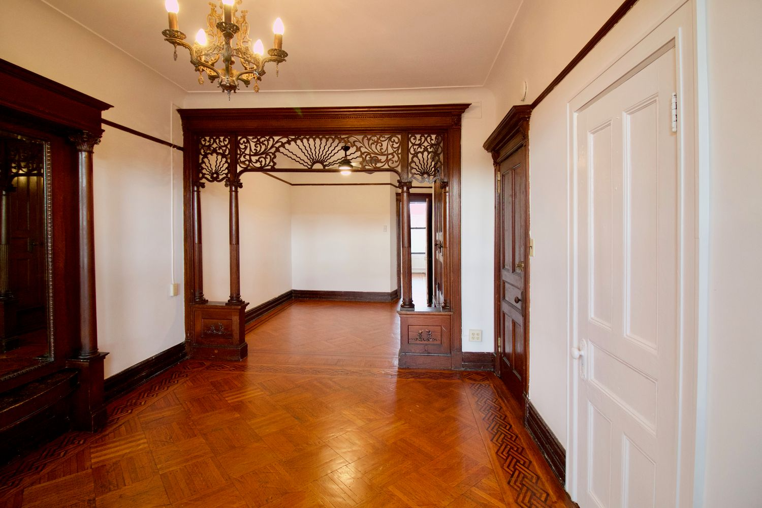 parlor with wood floor, pier mirror and fretwork screen framing entry to middle parlor