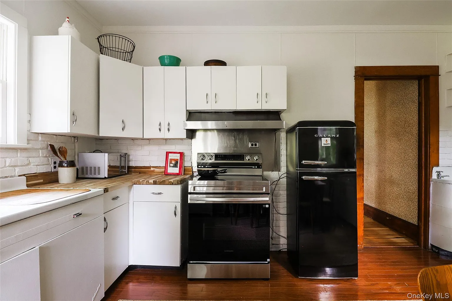 kitchen with vintage white metal cabinets, exposed brick painted white, black appliances