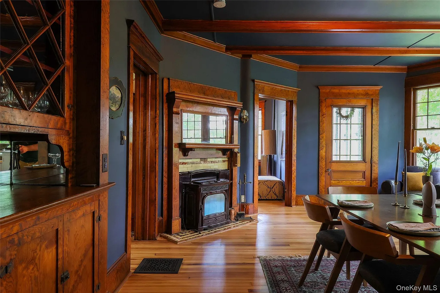 dining room with dark blue walls, beamed ceiling, built-in china cabinet, mantel