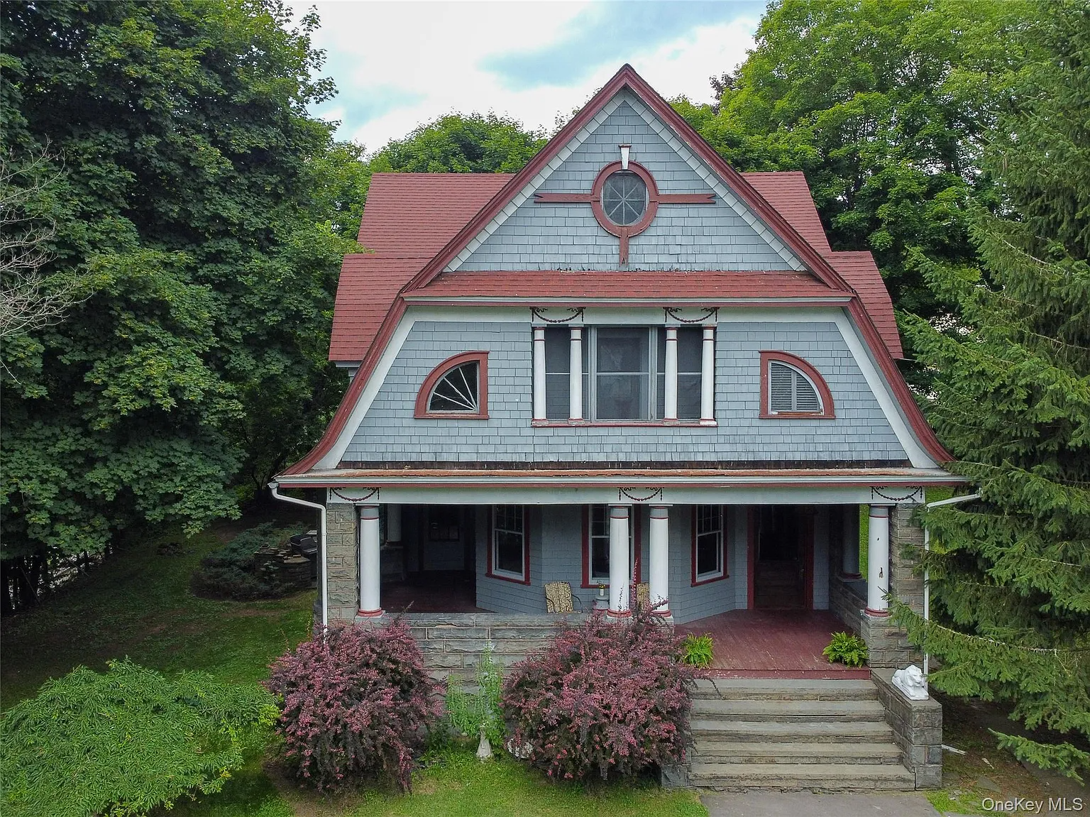 a shingle style house with blue shingles, red trim and a front porch
