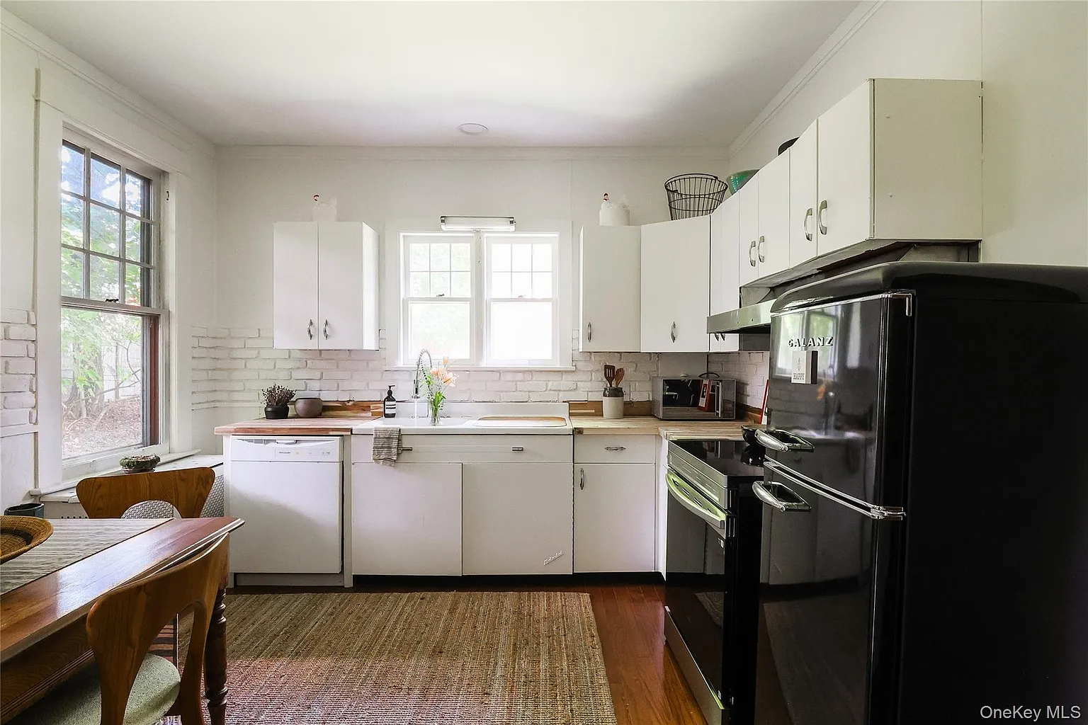 kitchen with vintage white metal cabinets, exposed brick painted white, black appliances