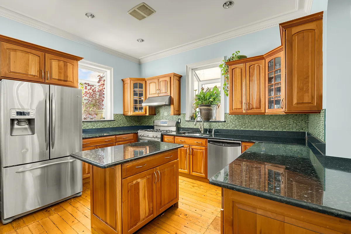 kitchen with green mosaic tile backsplash, wood cabinets, black countertops