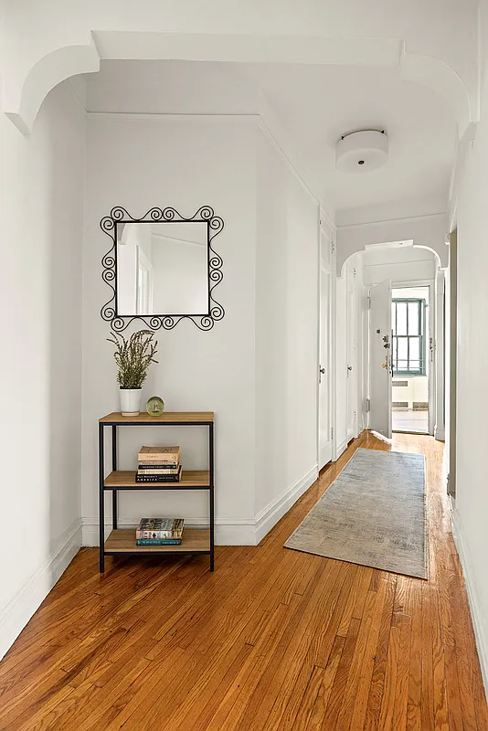 hall to entry with wood floor, white walls, arched doorway