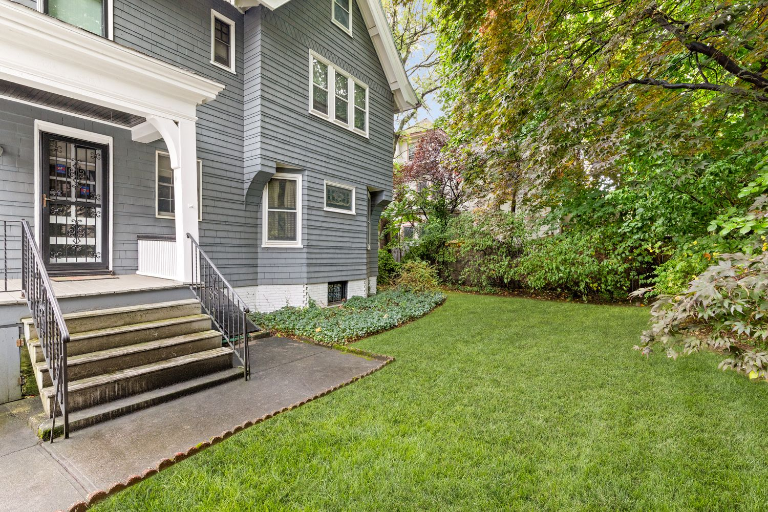 rear facade of the house showing a small rear porch and a sideyard with lawn, shrubs and trees