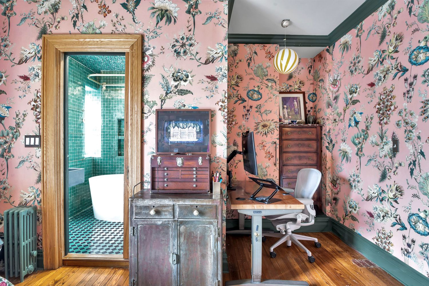 bedroom with oversized pink, floral wallpaper and view into an ensuite bath with green tiles