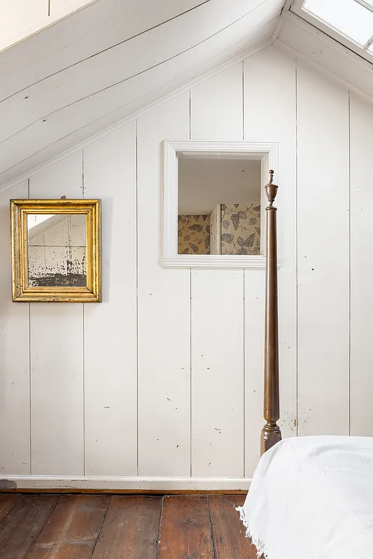 bedroom with white painted panelling, window in wall to office