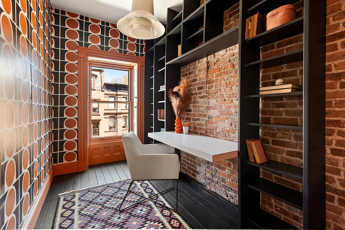 narrow bedroom set up as an office with graphic black and orange wallpaper, exposed brick wall