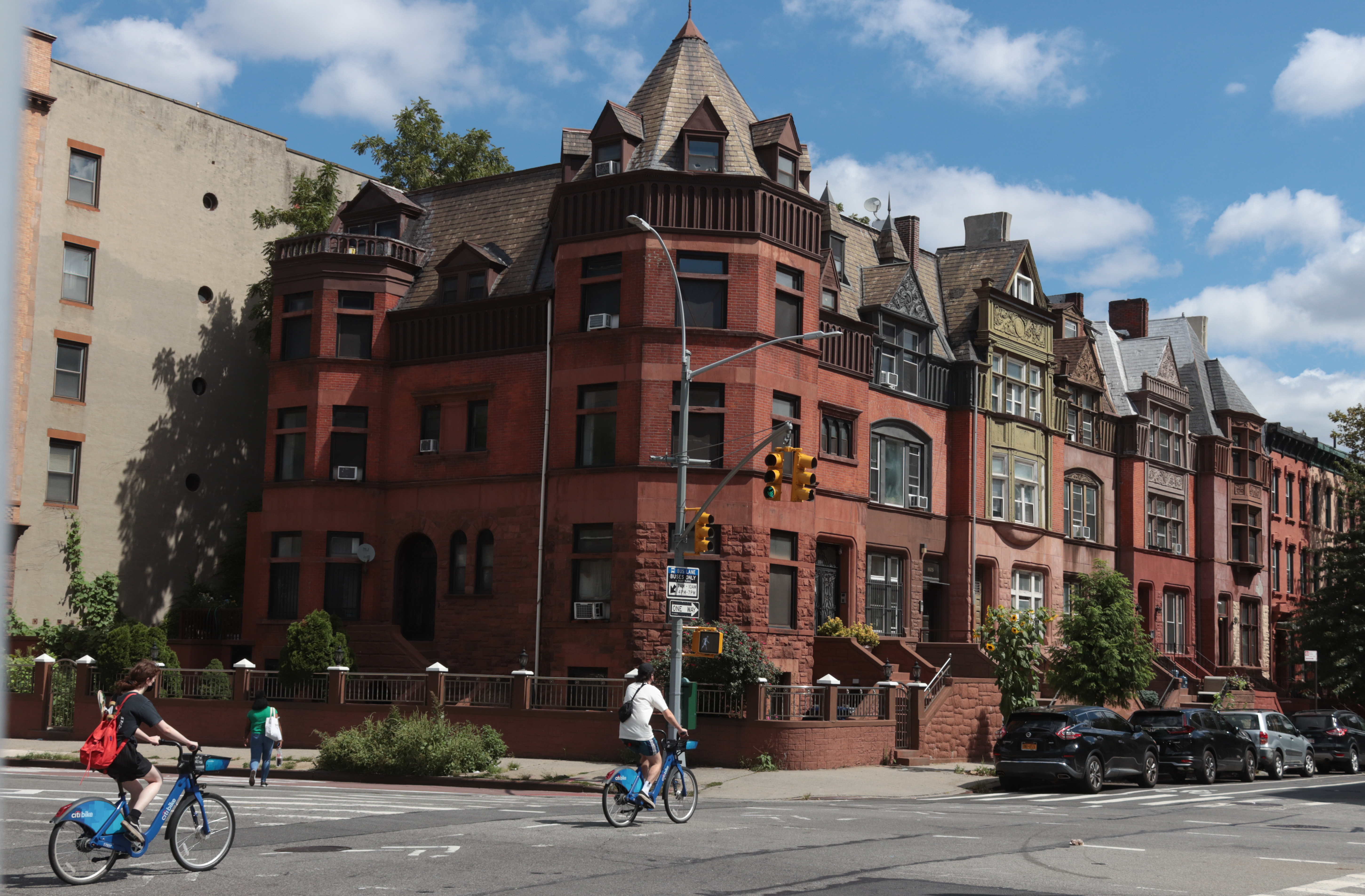 people on bikes ride by large brick dwellings